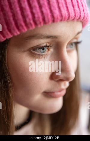 Kopfschuss einer friedlichen jungen Frau im Hut, die wegschaute, während sie im Zimmer mit Sonnenlicht stand Stockfoto