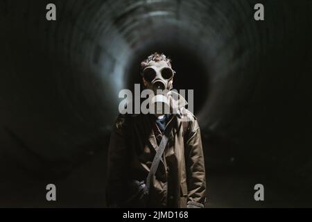 Nicht erkennbarer männlicher Entdecker in Gasmaske, der während der Apokalypse einen dunklen unterirdischen Tunnel mit Taschenlampe beleuchtet Stockfoto