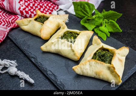 Köstliches libanesisches Essen, Spinat-Sfiha auf schwarzem Schieferstein-Hintergrund und traditioneller libanesischer turb Stockfoto