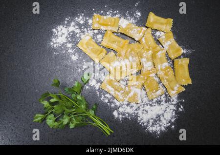 Ravioli und Petersilie in Pulverform mit Weizenmehl auf dem Granit Tisch Stockfoto