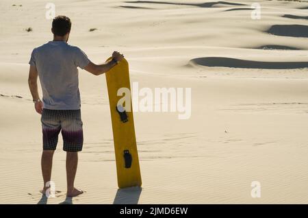 Junger Mann auf seinem Rücken an den Sanddünen suchen, Vorbereitung sandboarding zu üben. Stockfoto