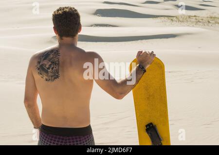 Junger Mann auf seinem Rücken an den Sanddünen suchen, Vorbereitung sandboarding zu üben. Stockfoto