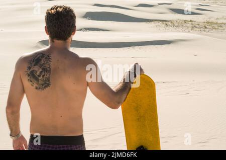 Junger Mann auf seinem Rücken an den Sanddünen suchen, Vorbereitung sandboarding zu üben. Stockfoto