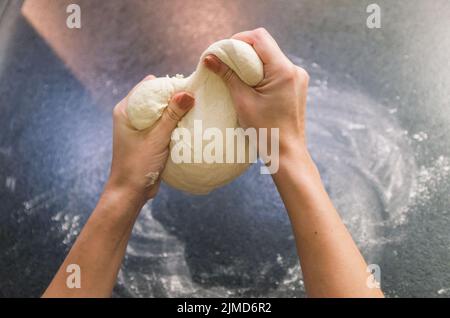 Frau Vorbereitung Pizza Teig auf schwarzem Granit Tisch Stockfoto