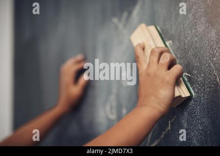 Versuchen wir es noch einmal. Ein nicht erkennbarer Junge, der den Staubwedel verwendet, um eine Tafel zu reinigen. Stockfoto