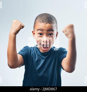 Aufwachsen mit einem starken Selbstwertgefühl. Studioaufnahme eines niedlichen kleinen Jungen, der seine Muskeln vor einem grauen Hintergrund beugend. Stockfoto