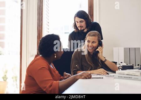 Eine Gruppe von Geschäftsleuten, die aufgeregt sind, während sie in einem Büro einen Anruf tätigen, ist begeistert. Stockfoto