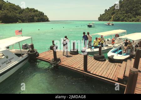 Besucher, die aus den Booten steigen, kommen an einem Steg auf Pulau Sapi (Sapi Island) an, einem Teil des Tunku Abdul Rahman Parks in Sabah, Malaysia. Stockfoto