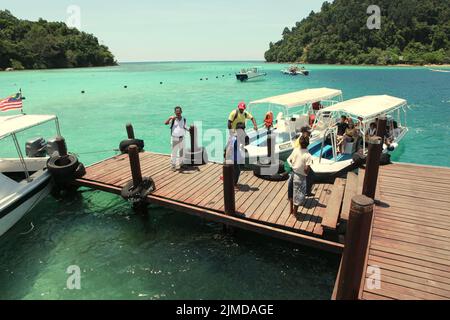 Besucher, die aus den Booten steigen, kommen an einem Steg auf Pulau Sapi (Sapi Island) an, einem Teil des Tunku Abdul Rahman Parks in Sabah, Malaysia. Stockfoto