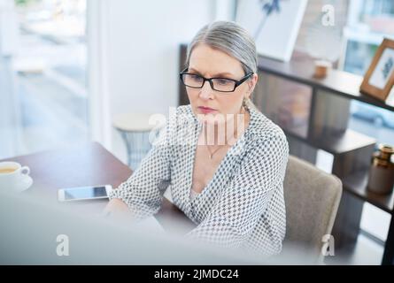 Konzentriert sich darauf, Perfektion in ihre Arbeit zu bringen. Eine reife Geschäftsfrau, die an einem Computer in einem Büro arbeitet. Stockfoto