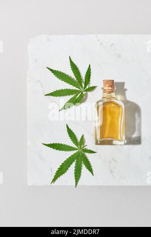 Medizinisches Marihuanaöl und grüne Cannabisblätter auf hellgrauem Marmorhintergrund. Stockfoto