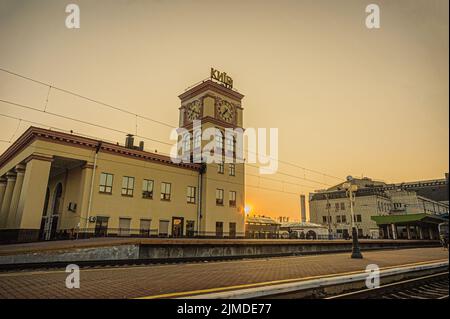 Vorstadtbahnhofsgebäude mit Uhrturm und Kiew-Pasazhyrskyi Hauptbahnhof in den Strahlen der aufgehenden Sonne. Stockfoto