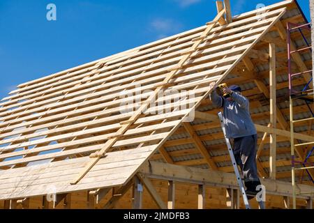 Der ältere grauhaarige Baumeister sammelt den Rahmen eines hölzernen Landhauses Stockfoto