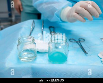 Sterile chirurgische Instrumente und Glasbehälter mit Lösungen auf dem Tisch während eines chirurgischen Eingriffs. Stockfoto