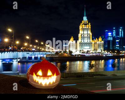 Halloween Kürbis auf dem Hintergrund der Nachtstadt. Mehrstöckige Gebäude und Wolkenkratzer. Verschwommene farbige Lichter werden reflektiert Stockfoto