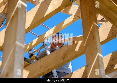 Der ältere grauhaarige Baumeister sammelt den Rahmen eines hölzernen Landhauses Stockfoto