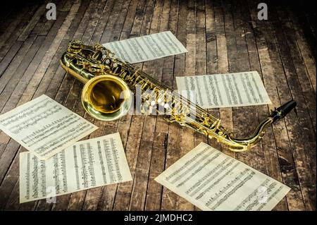 Schönes gelbes Saxophon und Papier mit Noten auf einer alten Holzbühne Stockfoto