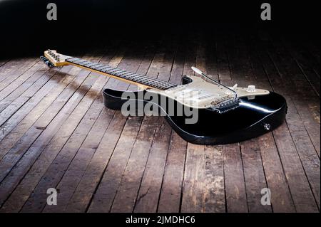 Schwarz-weiße E-Gitarre mit gelbem Stempel liegt auf einer Holzbühne Stockfoto