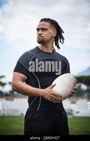 Hes bereit, Rugby zu spielen, wie der Profi, der er ist. Ein hübscher junger Rugby-Spieler hält einen Rugby-Ball, während er auf dem Feld steht. Stockfoto