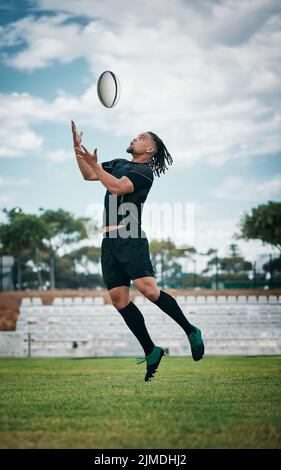 Der Ball ist sein zu haben. Ganzkörperschuss eines hübschen jungen Rugby-Spielers, der mitten in der Luft einen Ball auf dem Spielfeld fängt. Stockfoto