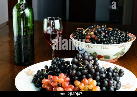 Frisch geerntete rote Trauben und schwarze Trauben in Keramikplatte mit Rotwein im Glas. Stockfoto