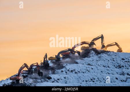 Silhouetten vieler Bagger, die auf einem riesigen Berg in einer Müllhalde arbeiten Stockfoto