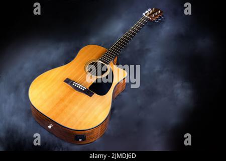 Akustische klassische gelbe 6-saitige Gitarre mit schwarzem Schlagbrett in Rauch auf schwarzem isolierten Hintergrund Stockfoto