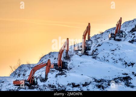 Silhouetten mehrerer Bagger, die auf einem riesigen Berg in einer Müllhalde vor dem Hintergrund arbeiten Stockfoto