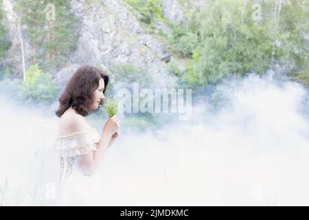 Schönes Mädchen mit dunklen Haaren im Nebel mit Blumen. Stockfoto