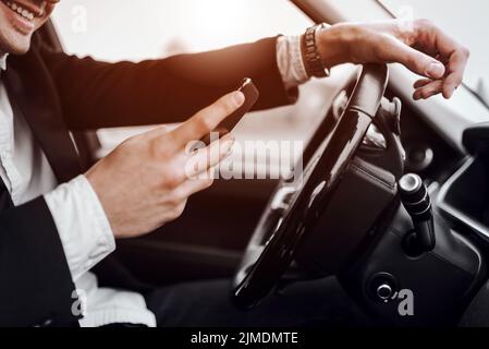Lächelnder junger Mann hält Handy im Auto Stockfoto