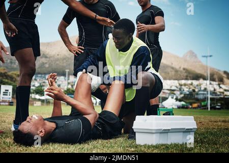 Das sieht aus wie eine schwere Verletzung. Ein junger Rugby-Spieler erhält erste Hilfe auf dem Feld. Stockfoto