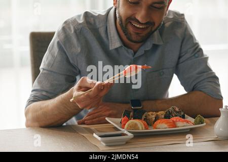 Glücklicher Mann mit Essstäbchen und leckerem Sushi im japanischen Restaurant Stockfoto