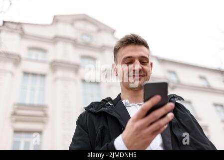 Lächelnder Typ tippt auf seinem Handy auf der Straße Stockfoto