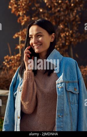 Eine ziemlich langhaarige Dame, die in einer herbstlichen Gasse per Mobiltelefon kommuniziert Stockfoto