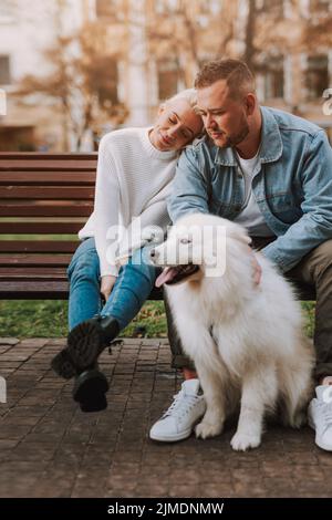 Paar, die sich auf der Bank ausruhen und sich um ihren Hund kümmern Stockfoto