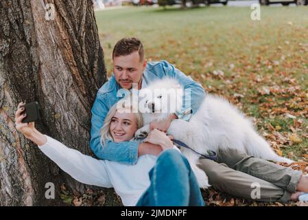Glückliches junges Paar mit Hund, der Spaß im Park hat Stockfoto