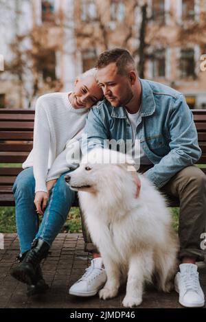 Glückliches Paar, das sich auf der Bank ausruhte und sich um ihren Welpen kümmerte Stockfoto