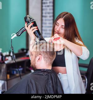 Frau Friseur trocknet das Haar im Salon zu Mann Stockfoto