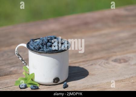 Frische Geißelbeeren mit Blättern auf Holztisch Hintergrund. Landwirtschaft, Gartenbau, sommerliches Erntekonzept Stockfoto