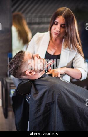 Friseurin schneidet im Friseursalon den Bart des Mannes Stockfoto