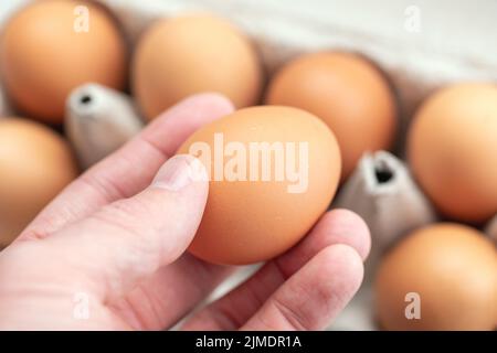 Ein frisches Ei von der Hand aus dem Papiertablett holen, gesundes Esskonzept Stockfoto