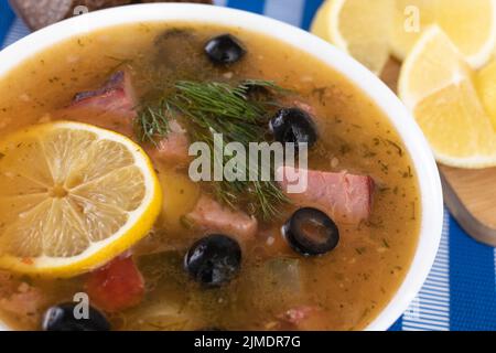 Traditionelle russische Suppe Soljanka mit Fleisch, Würstchen, gesalzene Gurken auf einer Schüssel gekocht. Schwarzbrot, Zitrone, Oliven und Toma Stockfoto