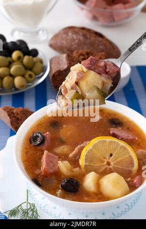 Traditionelle russische Suppe Soljanka mit Fleisch, Würstchen, gesalzene Gurken auf einer Schüssel gekocht. Schwarzes Brot, Zitrone, Olive und Toma Stockfoto