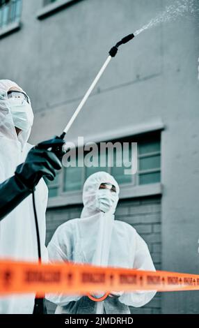 Mitarbeiter im Gesundheitswesen, die Hazmat-Anzüge tragen und ein Gebäude während einer covid Pandemie desinfizieren. Ersthelfer sprühen Virenschutzdesinfektionsmittel oder Stockfoto