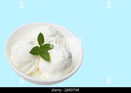 Weiße Schale mit weißem Eis und grünem Blatt isoliert auf blauem Hintergrund. Ort für Ihren Text oder Inhalt. Stockfoto