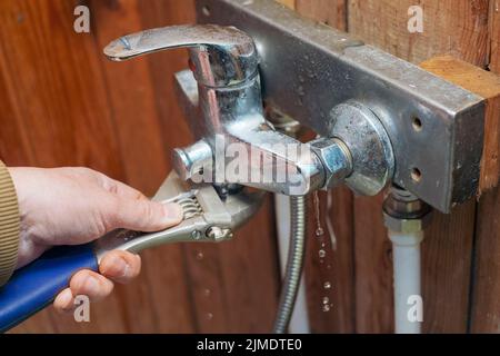 Eine Hand mit einem Schraubenschlüssel, der undichten Hahn fixiert, Nahaufnahme in Innenräumen Stockfoto