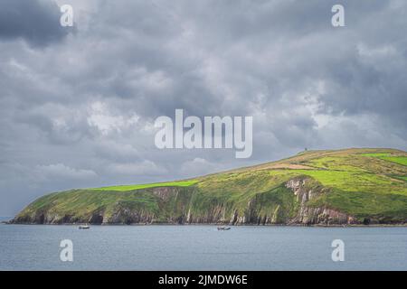 Fischerboote, die nach Dingle zurückkehren, mit grünen Feldern auf hohen Klippen Stockfoto