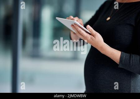 Noch viel mehr in mobiler Form. Nahaufnahme einer Schwangeren Geschäftsfrau, die in einem Büro ein digitales Tablet benutzt. Stockfoto