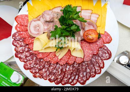 Ein Teller mit kalten Vorspeisen mit verschiedenen Würstchen, Fleisch und Käse. Grünpflanzen und Tomaten. Stockfoto