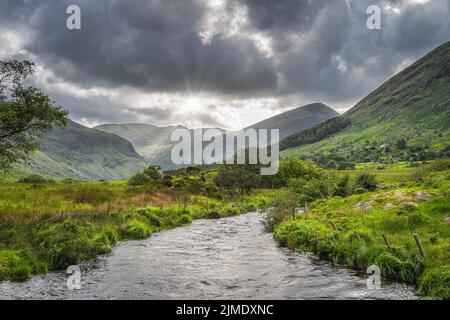 Der Fluss fließt durch das wunderschöne Black Valley mit dem dramatischen Himmel und dem Sonnenstern Ring of Kerry Stockfoto